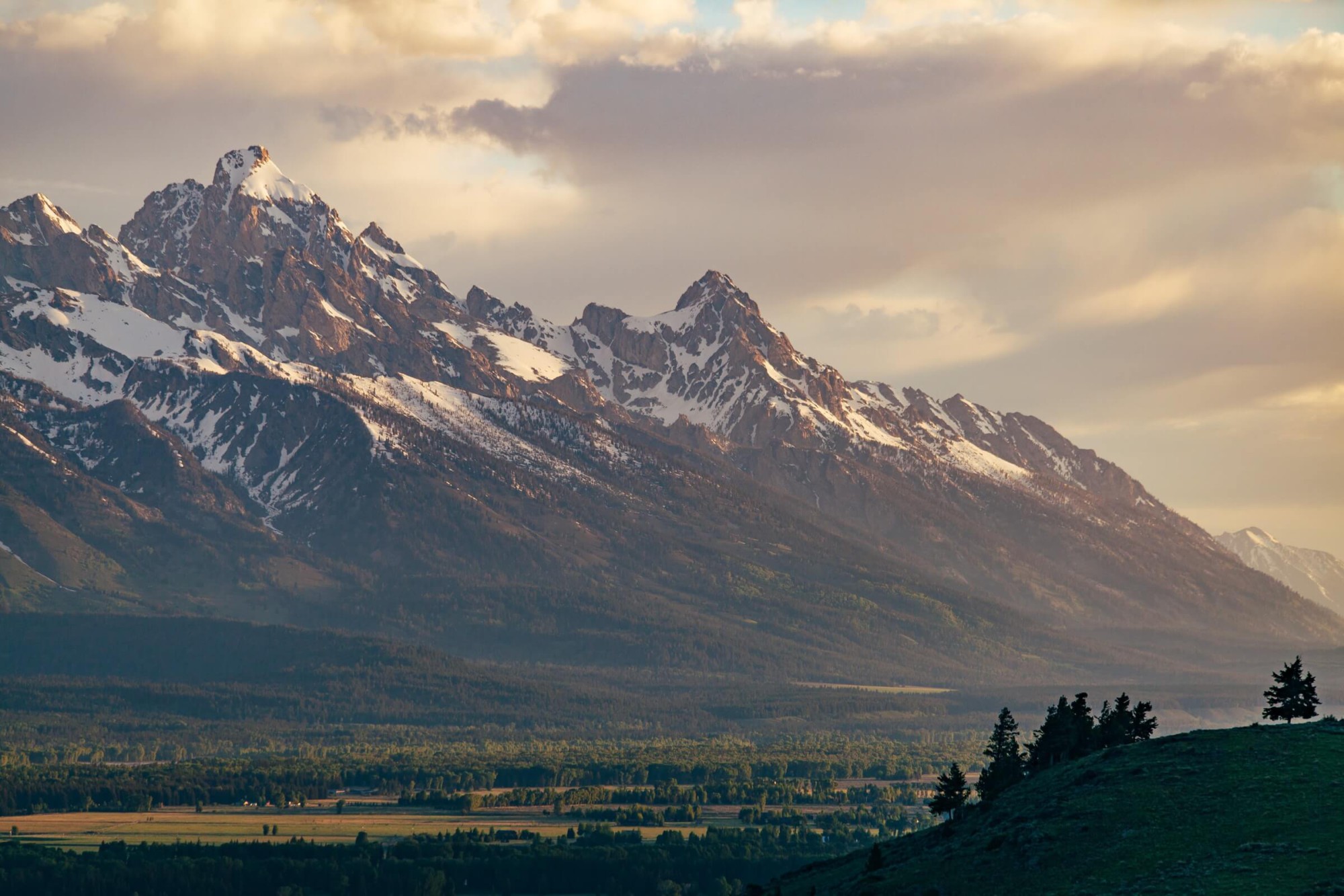 The Tetons are half-covered with snow on a cloudy day.