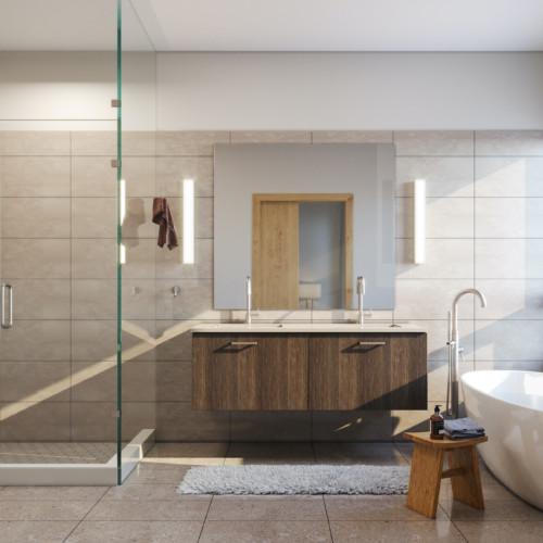 Natural light beams into a bathroom with a dark wood vanity, large white bathtub, and a beige, tiled wall.