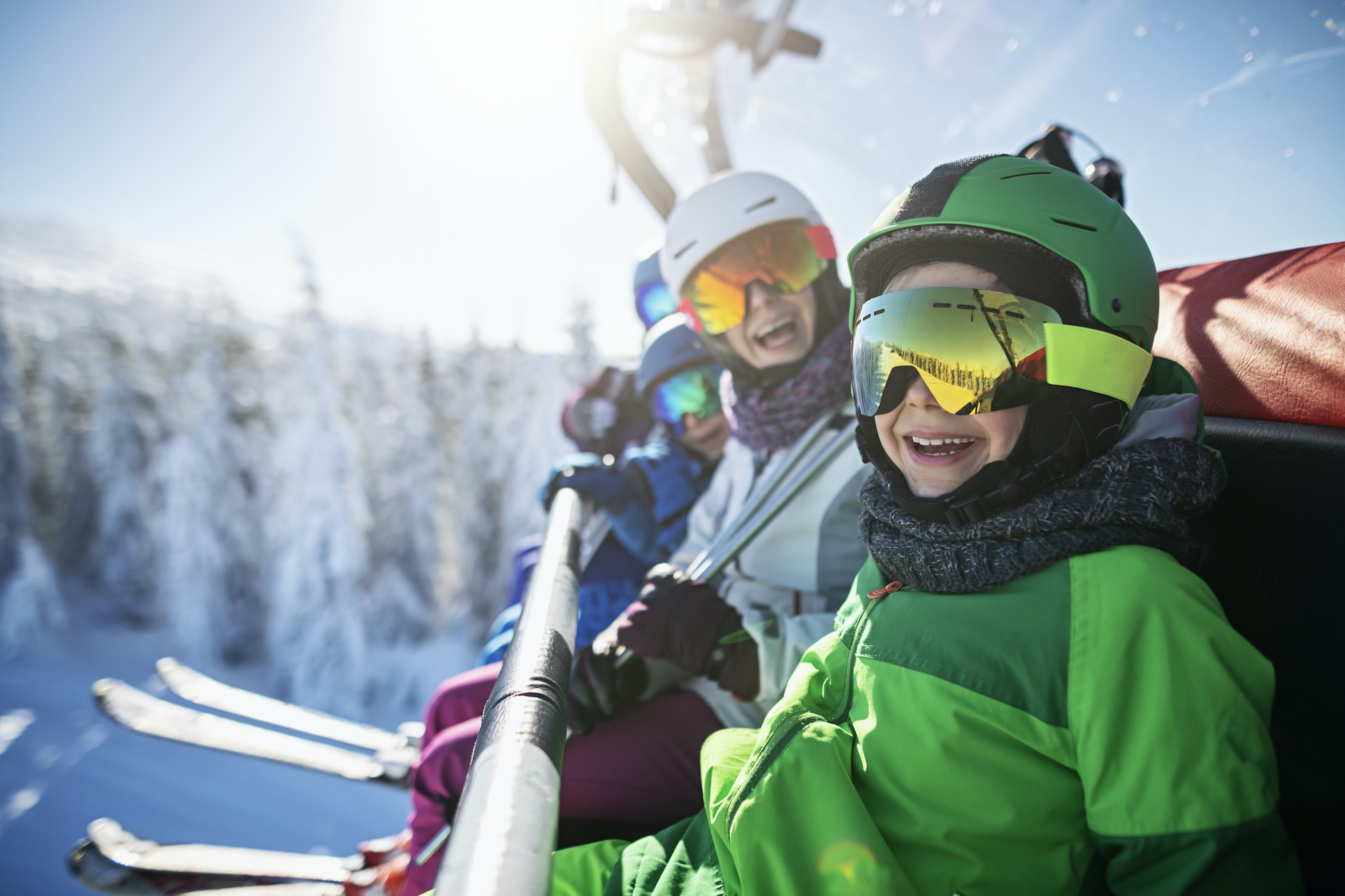 A happy family sits on a chairlift while enjoying a day skiing.