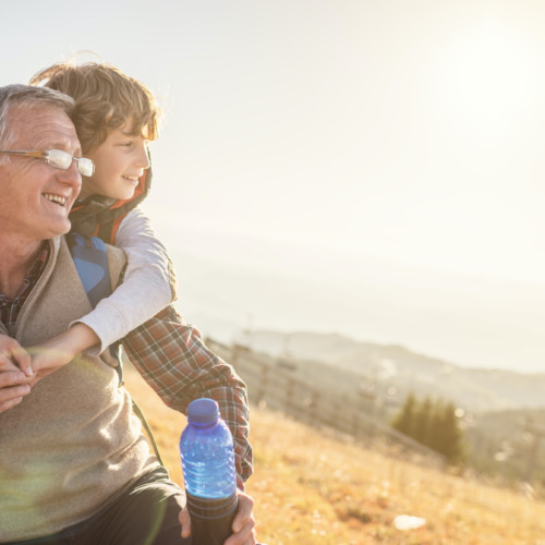 A happy father carries his son on his back while hiking.