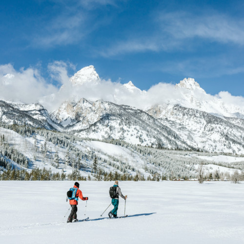 Two skiers tour across a flat field at the base of the Teton mountains.