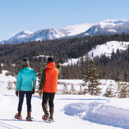 A couple out snowshoes on a groomed trail on a bluebird day in the mountains.