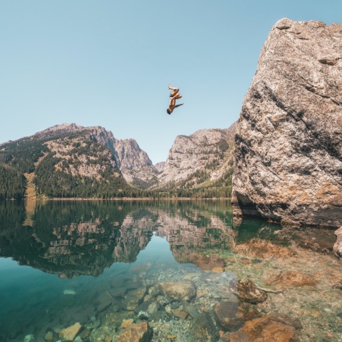 An adventurer backflips into Phelps Lake on a summer day in Grand Teton National Park.