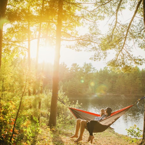 A couple enjoys a lakeside hang while sitting in a hammock.