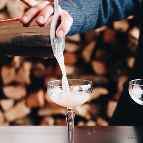 A bartender pours a craft cocktail through a strainer into a fancy class.