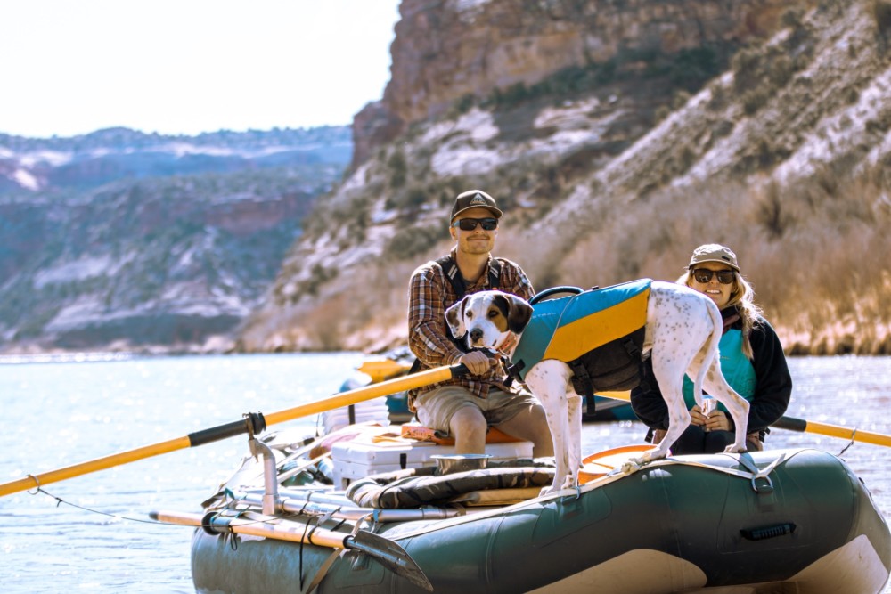 A couple and a dog float down a river canyon on an inflatable raft.