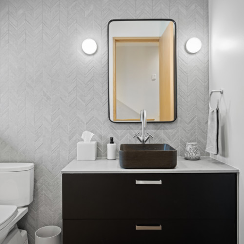 A half bathroom with a black vanity and light grey tiled wall.