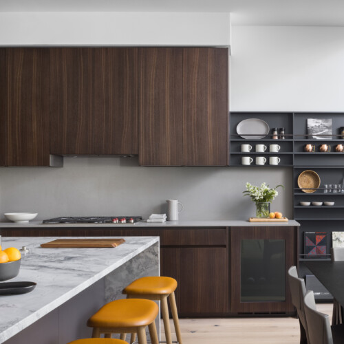 A luxurious and modern kitchen with walnut cabinets, black shelves, and a marbled countertop.